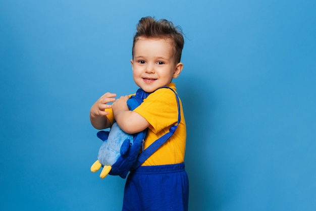 Um pequenino fofo abraços com sua mochila em um fundo azul. garoto engraçado