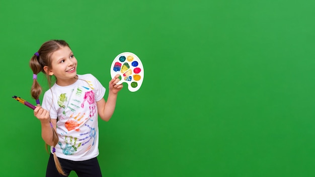 Um pequeno artista com uma paleta de cores aponta para seu anúncio em um fundo verde isolado Cursos de arte para crianças