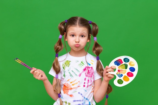 Um pequeno artista com uma paleta multicolorida de tintas e pincéis para desenhar em um fundo verde isolado Cursos de arte para crianças em idade escolar