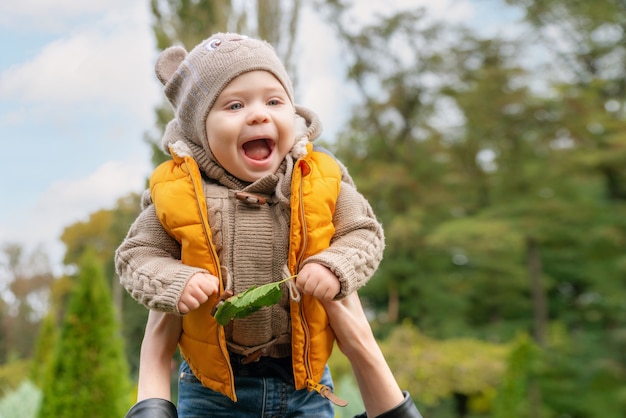 Um pequeno bebê jogando no ar ao ar livre no outono park. Mamãe joga seu bebezinho sorridente para o céu. Família feliz.