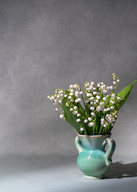 Um pequeno buquê de flores frescas da primavera Lírios do vale em um vaso leve isolado em um fundo cinza Muito espaço para texto ainda vida cartão postal presente