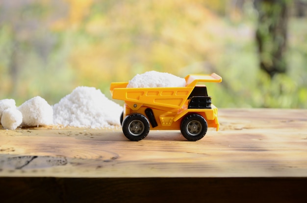 Um pequeno caminhão de brinquedo amarelo é carregado com uma pedra de sal branco ao lado de uma pilha de sal.