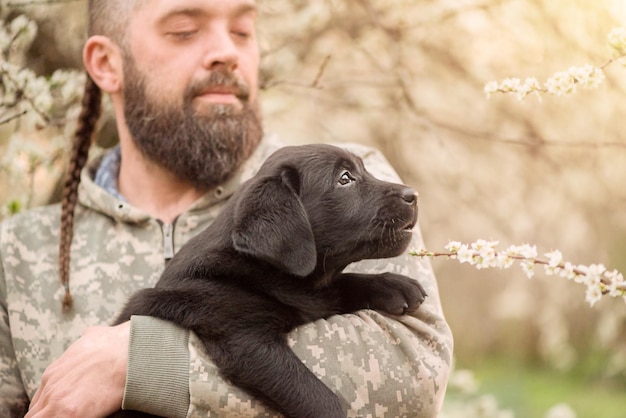 Um pequeno filhote de labrador retriever preto Um cachorro nos braços de um homem barbudo