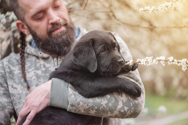 Um pequeno filhote de labrador retriever preto Um cachorro nos braços de um homem barbudo