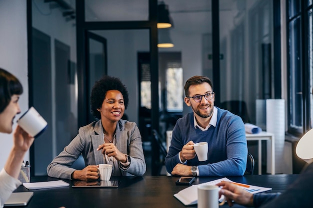 Um pequeno grupo feliz de colegas multirraciais está tomando café no espaço de coworking