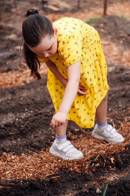 Um pequeno jardineiro ajuda os pais a plantar verduras e jardins de uma menina no quintal dos fundos do jardim