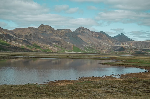 Foto um pequeno lago no meio de uma montanha com montanhas ao fundo.