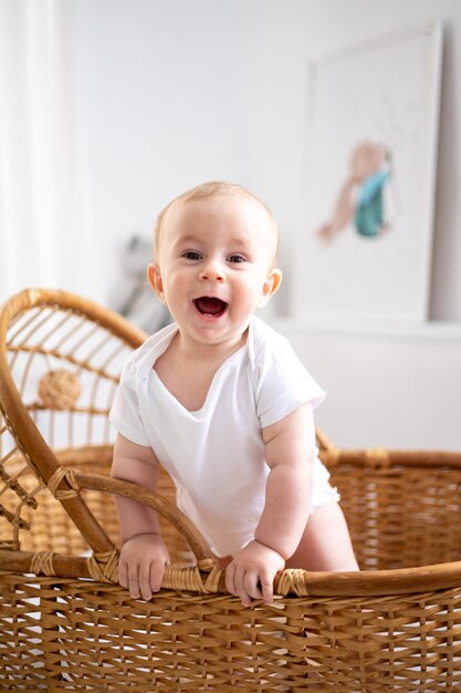 Foto um pequeno menino sorridente em um terno branco em um berço de rattan de vime em um quarto de crianças brilhante sorri olha para a câmera o interior do quarto das crianças o sono das crianças