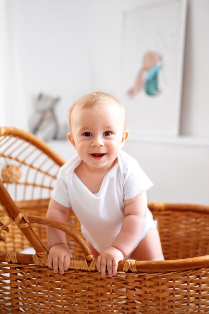 Foto um pequeno menino sorridente em uma roupa branca em um berço de rattan de vime em um quarto de criança brilhante sorri olha para a câmera o interior do quarto das crianças o sono das crianças