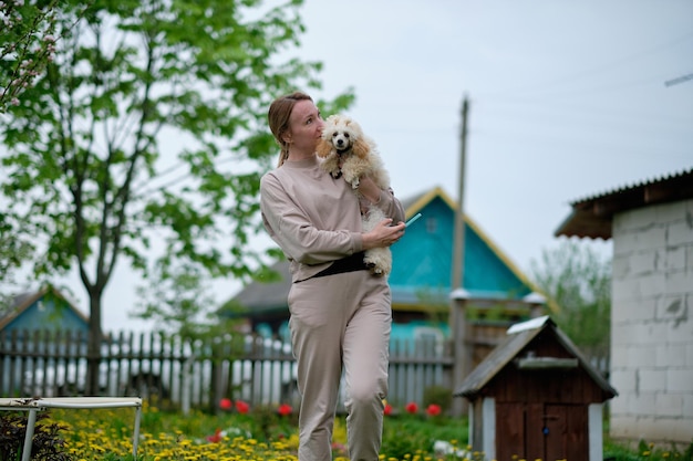 Um pequeno poodle de damasco nos braços de uma mulher no jardim