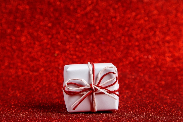 Foto um pequeno presente branco em um vermelho brilhante, lantejoulas nas laterais. o conceito de dia dos namorados.