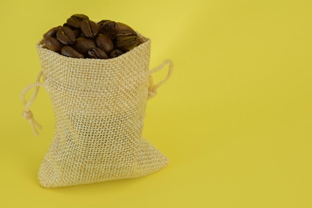 Um pequeno saquinho com grãos de café fica em pé sobre um fundo amarelo