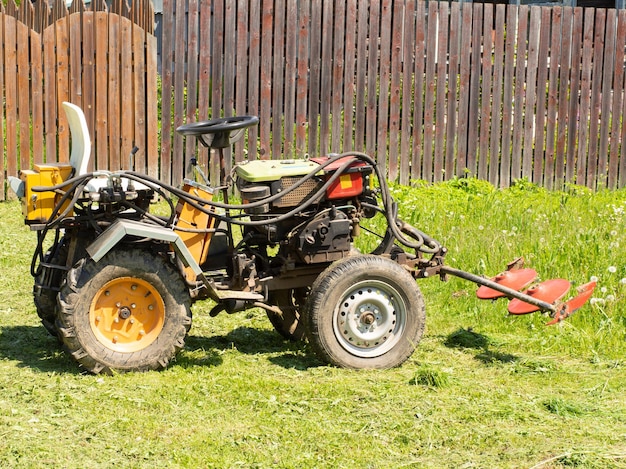 Um pequeno trator com um acessório de cortador para grama em pé em uma máquina agrícola agrícola