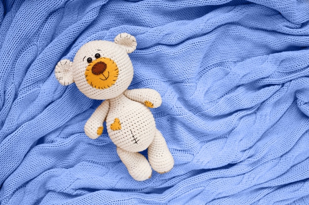 Foto um pequeno urso de brinquedo de bebê amigurumi de malha está em um cobertor azul