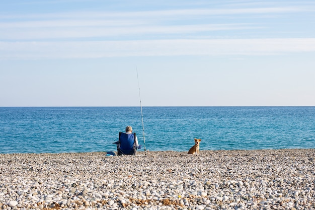 Um pescador e um cachorro estão sentados à beira-mar