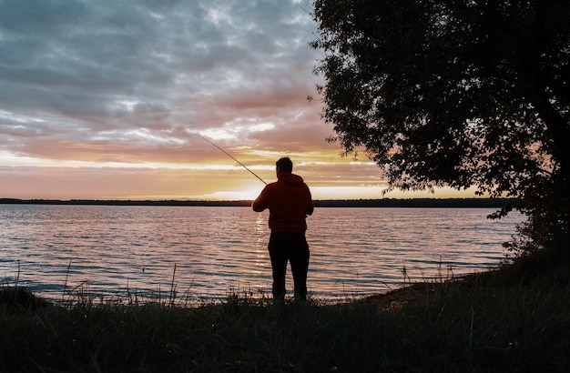 Um pescador está pescando ao pôr do sol em um grande lago bonito