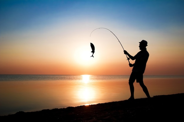 Um pescador feliz pescando peixes à beira-mar em uma viagem de silhueta da natureza