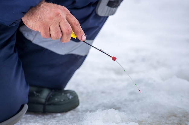 Um pescador na pesca de inverno senta-se com vara de pescar por buraco