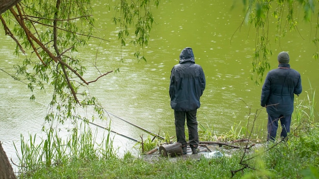 Um pescador pesca no lago em uma vara de pescar durante a chuva.