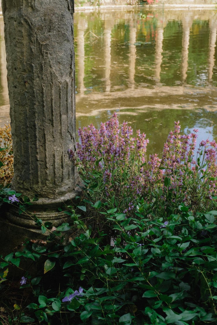 Foto um pilar de pedra com flores na frente de uma lagoa