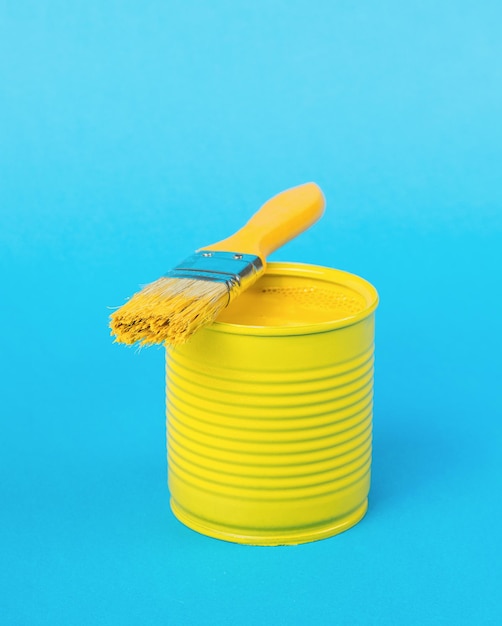 Um pincel deitado em uma jarra com tinta amarela sobre fundo azul Cores de tendência Conceito mínimo de seleção interior