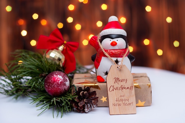 Um pinguim de brinquedo com uma nota com o texto Feliz Natal e Feliz Ano Novo em um fundo de bokeh