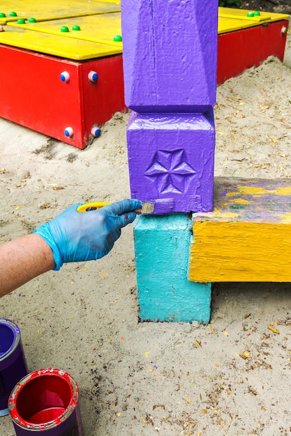Um pintor pinta um poste de madeira com esmalte alquídico em um parque infantil