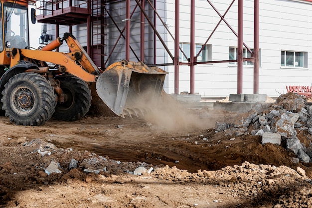 Um poderoso carregador frontal em um canteiro de obras resolve a batalha após o desmantelamento de estruturas de concreto armado. Movendo o solo com equipamentos de construção. Escavações.