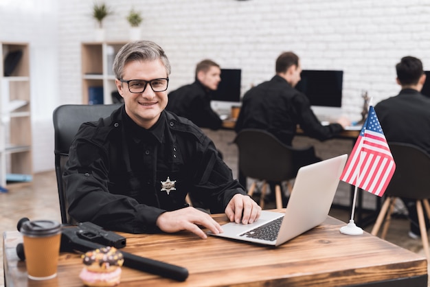 Um policial trabalha para um laptop em uma delegacia de polícia.