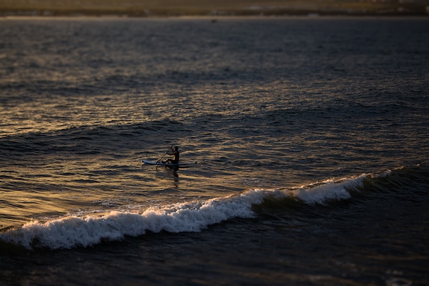 Um pôr do sol brilhante, raios caindo na superfície do mar, grandes ondas de espuma indo para as rochas e surfistas de sup, paisagens maravilhosas na cidade resort de gelendzhik