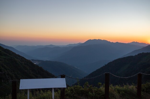 Um pôr do sol cênico nas montanhas com luz solar, bela luz. Paisagem de verão à noite em um vale com horizonte, céu, grama, flores. O conceito de viagem