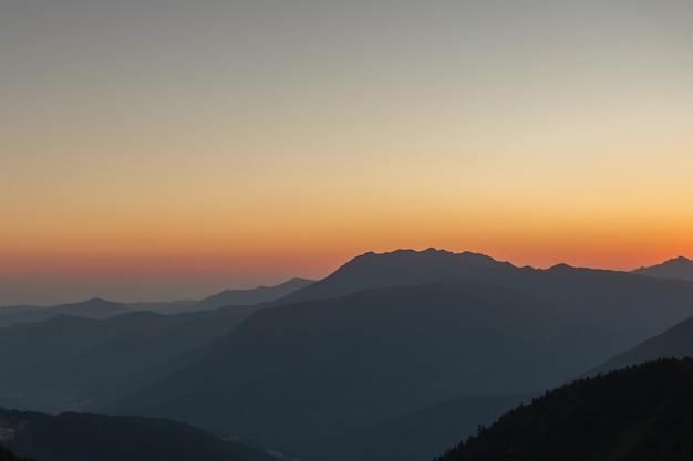 Um pôr do sol cênico nas montanhas com luz solar, bela luz. Paisagem de verão à noite em um vale com horizonte, céu, grama, flores. Panorama da natureza do fundo da imagem