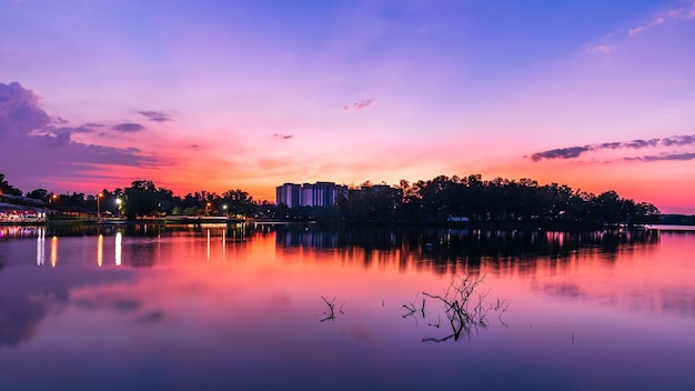 Um pôr do sol roxo sobre um lago com um rio e um prédio ao fundo.