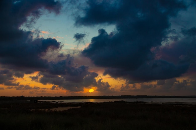 Foto um pôr do sol sobre a água com algumas nuvens no céu