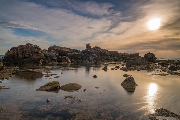 Um pôr do sol sobre a água com pedras e o pôr do sol atrás dele