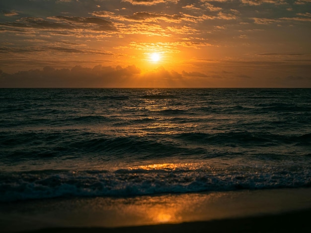 Foto um pôr-do-sol sobre o oceano com uma praia e o sol a pôr-se atrás dele