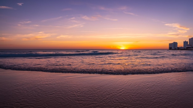 Um pôr-do-sol sobre o oceano com uma praia e o sol a pôr-se.