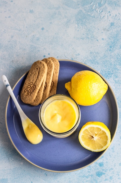 Um pote de coalhada de limão ou creme e biscoitos num prato azul.