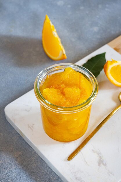 Um pote de laranjas está sobre uma tábua branca ao lado de uma pequena fatia de laranja.