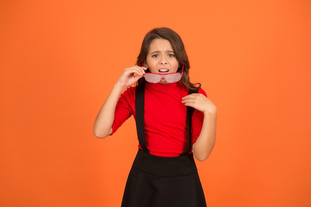 Um pouco chateado aluno de aparência legal fundo laranja bonito e elegante criança pequena menina uniforme escolar óculos de festa para diversão conceito de moda infantil Ficar focado com óculos