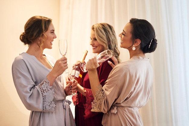 Um pouco de champanhe fará foto recortada de uma linda jovem noiva e suas damas de honra tomando champanhe em seu camarim antes do casamento