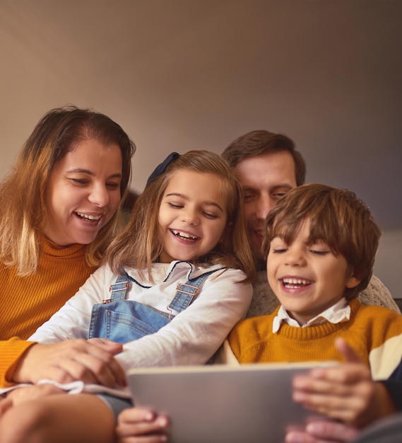 Um pouco de diversão em família na internet Foto recortada de uma jovem família afetuosa de quatro pessoas usando um tablet digital enquanto está sentado no sofá em casa