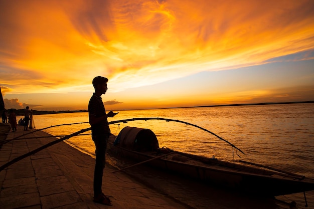 Um povo em pé no mar contra o céu durante o pôr do sol