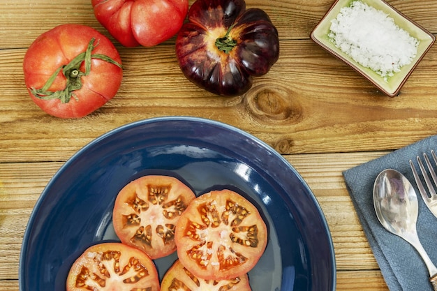 Um prato azul com fatias de tomate em algumas pranchas de madeira