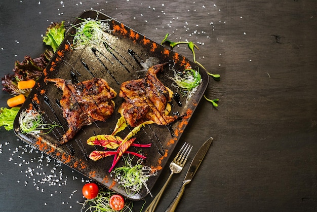 Um prato com carne de codorna assada com legumes em fundo preto