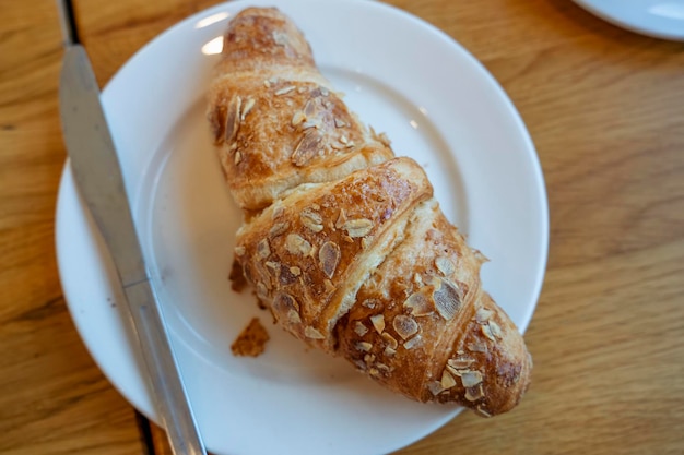 Um prato com croissant de amêndoa e faca em uma mesa em um café vista de cima