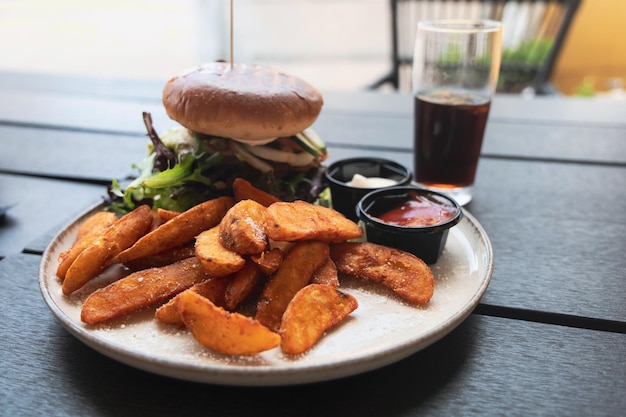 Um prato com hambúrguer e batatas fritas, ketchup, maionese e cola na mesa.