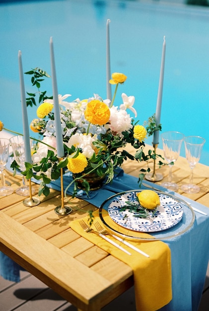 Um prato com um limão amarelo e um galho de oliva está em uma mesa festiva perto de um buquê de flores