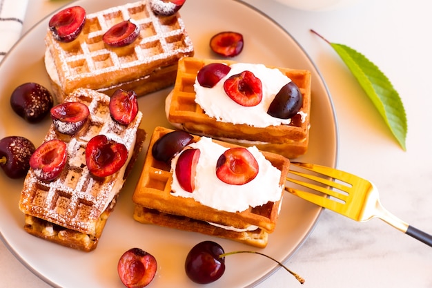 Um prato com waffles belgas recém-macios e cerejas com creme em uma mesa branca.