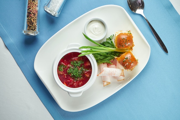 Um prato da culinária ucraniana - borsch de porco rica com pampushka, cebolinha e bacon (banha) em um prato branco sobre uma toalha de mesa azul